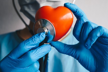 Person in OP-Kleidung hält eine Attrappe eines roten Herzens und ein Stethoskop hält